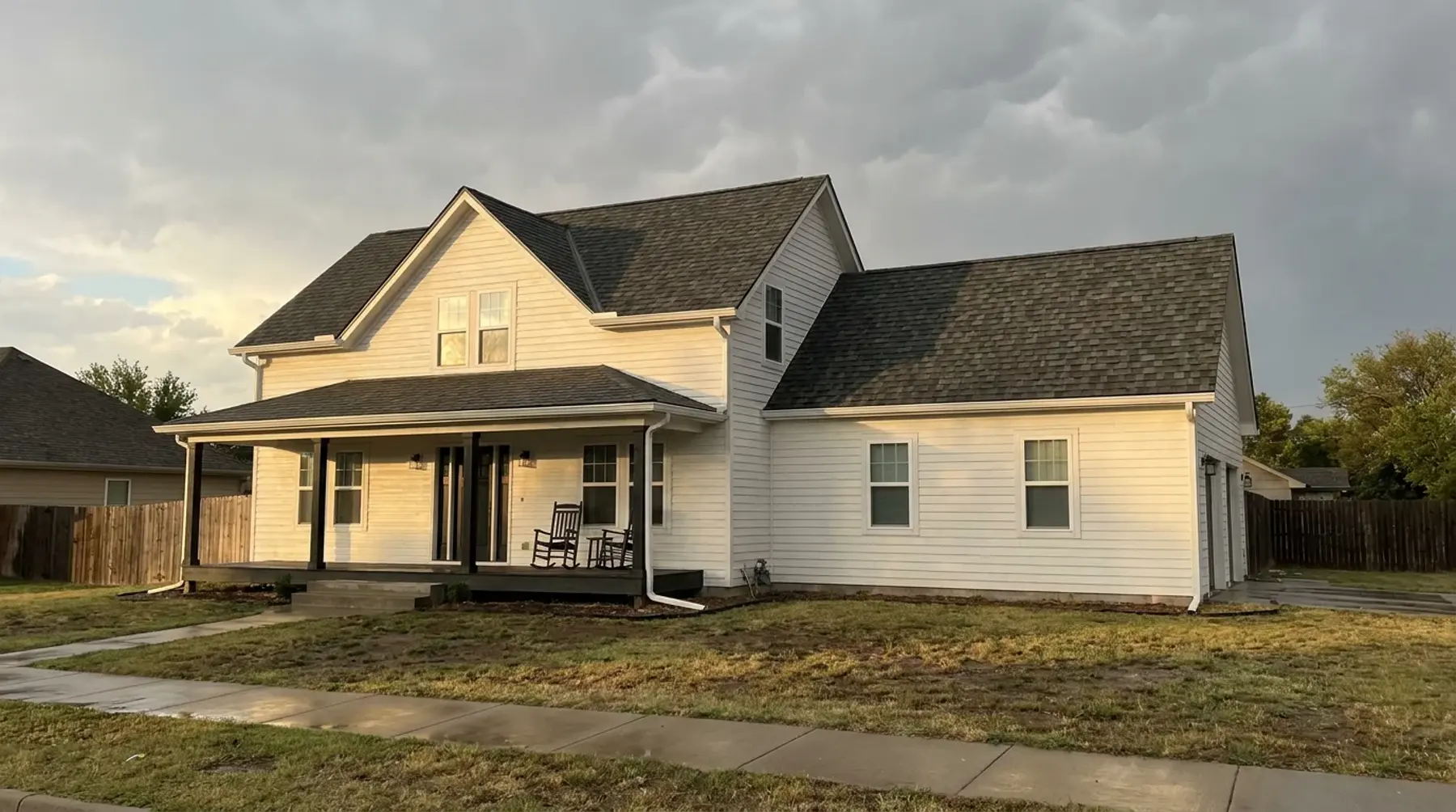 A white farmhouse with a new dark shingle roof under clearing storm clouds